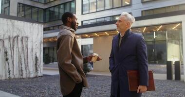 Two colleagues of different nationality and age are discussing business ideas in the open air near the entrance to a modern office building photo