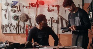Male blacksmith in work clothes shows his colleague an idea for a sketch on a clipboard, working together to design a future product in a workshop full of tools. in 4k, red komodo photo