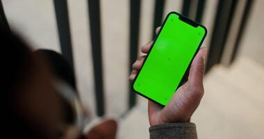 Mobile phone with a green screen in the hand of a man of African American appearance, filming from behind, his face is not visible. Copy space, mockup, chroma key. in 4k, red komodo photo