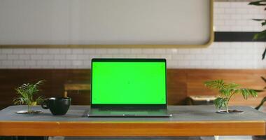 An open laptop with green screen stands on a table in a coffee shop. There are no people in the frame. Chroma key, copy space photo