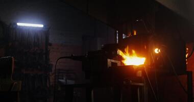 Blacksmith in protective gear and goggles takes an angle grinder and starts to cut off a part of a metal blank while working in a forge. 4k , red komodo photo