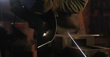 A blacksmith in protective equipment saws off a part of a metal stick using a flex, metal sparks fly in different directions, close up, no face, unrecognizable person. 4k , red komodo photo