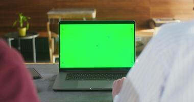 Two people sit at table in a cafe in front of an open laptop with a green screen. Filming from the back. Chroma key, copy space photo