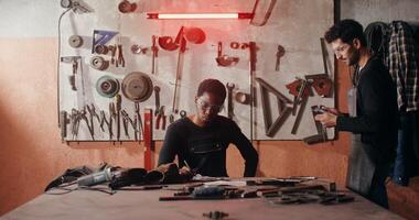 Two blacksmiths in work clothes drawing a sketch of a future product, working together and using a tablet to search for ideas, in a workshop full of working tools. in 4k, red komodo photo