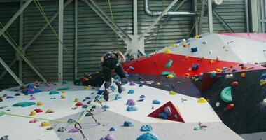 An athlete of European appearance descends from a climbing wall using a rescue rope and kicks off the wall. filming under artificial lighting in a modern gym photo