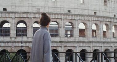 A young beautiful woman smiles while taking photos of the sights of Rome on a mobile phone, standing on an observation deck near the Coliseum. in 4k, red komodo.