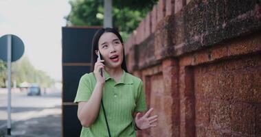 Cheerful young woman talks on the phone while walking on a sidewalk in the city. video