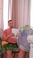 A man cools down under a fan on a hot day, escaping from the stuffiness and heat. It helps him to relax and recuperate. video