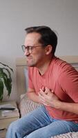 Vertical , Man on bed at home experiencing sharp chest pain, looking worried. Falling on back from heart attack or stroke. Concept. medical care, health. video