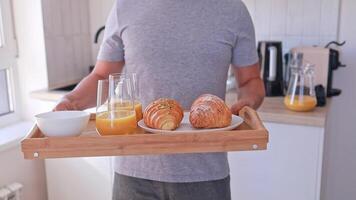 Close-up of a man holding a tray with breakfast with croissants and orange juice for himself and his wife. Breakfast in bed video