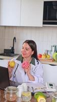 A nutritionist communicates with patients via computer at a table with fruits and vegetables. Consultation on healthy eating using a donut and an apple as an example. video