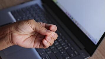 numbness in fingertips, close-up of hand squeezing numb fingers with laptop in background. Concept of hand numbness, nerve pain, carpal tunnel syndrome, or office syndrome from computer overuse video
