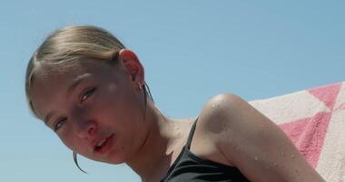 Young blond girl wearing black swimsuit lounging comfortably on beach towel, basking in warm summer sunlight and enjoying peaceful vacation moments with carefree expression video