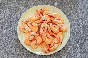 Cooked shrimps are arranged on a light green plate placed on a granite countertop, ready to be enjoyed as a delicious seafood meal or appetizer photo