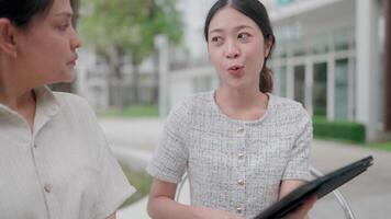 Two individuals engage in a focused conversation, utilizing a tablet for data analysis amidst a well-lit, contemporary urban setting. video
