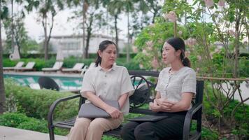 Two women talk in a quiet atmosphere, by an attractive pool and the surrounding greenery, creating a sense of peace. video