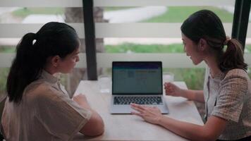 Two Colleagues Analyzing Data.Two female colleagues attentively analyze data on a laptop screen in a modern, well-lit workspace. A candid capture of collaboration and technology use video