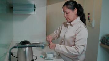 A woman is making tea in a simple yet practical setting. This image focuses on the daily ritual of making tea and provides an overview of daily life. video