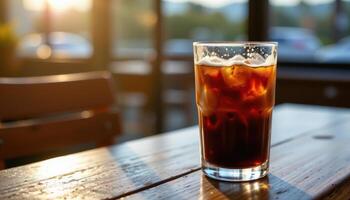 a glass of iced coffee with condensation, sitting on a wooden table in morning light. photo