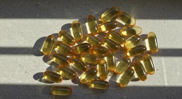 Pile of translucent yellow omega 3 fish oil capsules on a grey surface with sunlight photo