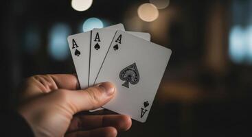 A hand holds three aces playing cards, including the ace of spades, against a blurred background. photo