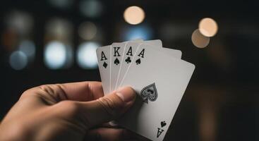 Hand holding a strong poker hand with three aces and a king against a dark background. photo