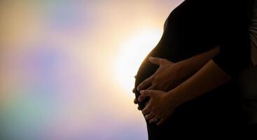Silhouette of a pregnant woman belly embraced by a man hands, symbolizing new life. photo