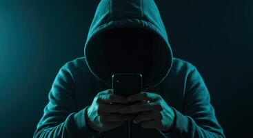 Anonymous hacker in a hoodie using a smartphone, symbolizing cyber security threats and online crime. photo
