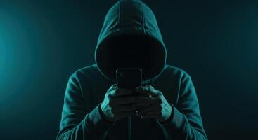 Anonymous person in dark hoodie using smartphone for cybercrime and digital security. photo