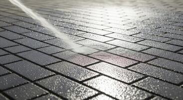Powerful water spray cleans dark grey brick pavement, creating a wet and reflective surface. photo