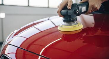 Professional car detailing, Person polishing the glossy red paint of a vehicle with an orbital machine. photo