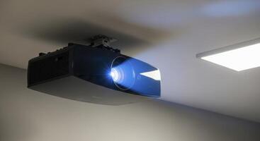 Sleek black projector mounted on a ceiling, casting a bright blue light in a modern room. photo