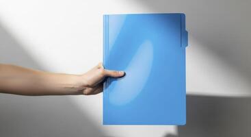 Fair skinned hand holding a vibrant blue plastic folder against a white background with shadows photo
