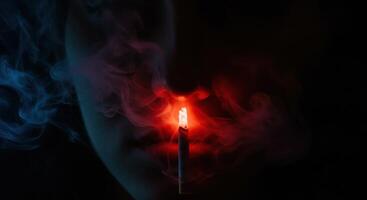 Glowing cigarette tip with red and blue smoke illuminating a shadowy figure in darkness. photo
