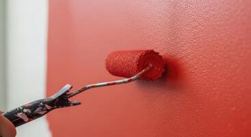 Close up of a paint roller applying vibrant red paint to a textured wall during home renovation. photo