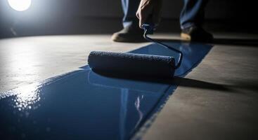 Man applying blue epoxy paint to a concrete floor with a roller for renovation project photo