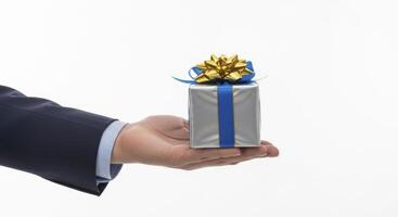 A businessman hand presents a silver gift box with a blue ribbon and gold bow. photo