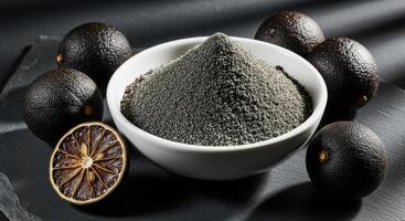Black lime powder in a white bowl with whole and sliced dried limes on a dark surface. photo