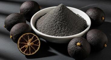 Black Limes and Dried Lime Powder in a Bowl on a Dark Surface for Culinary Use photo