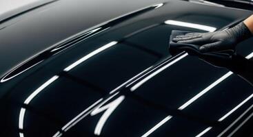 Professional hand polishing a black car hood for a perfect, glossy finish and deep shine photo