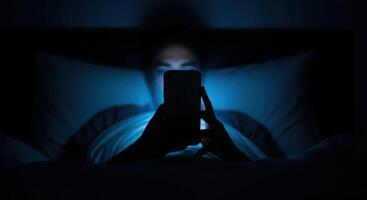 Adult using smartphone in bed at night with blue screen light illuminating face photo