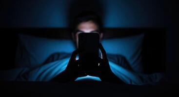 Man using smartphone in bed at night with blue screen light illuminating his face photo