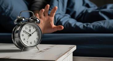 Hand Reaching for a Ringing Silver Alarm Clock on a Nightstand in the Morning photo