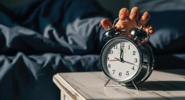 Hand reaching to turn off a classic silver alarm clock on a nightstand photo