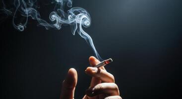 Hand holding a lit cigarette with smoke rising against a dark background photo