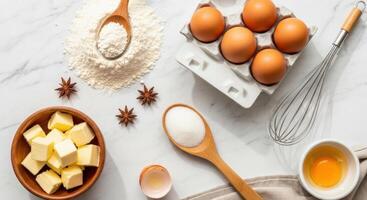 Baking ingredients flat lay with flour, eggs, butter, sugar, and whisk on marble surface photo
