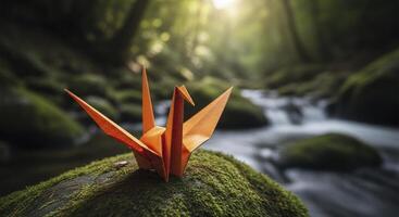 Vibrant orange origami crane on mossy rock in a tranquil forest with flowing stream photo