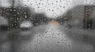 Rain droplets on a glass window with blurred street and vehicles in the background photo
