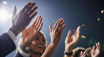 Diverse hands clapping enthusiastically at a celebratory event with bright lights and falling confetti. photo
