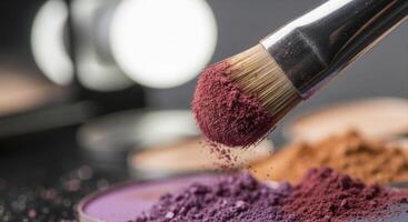 Close up of a makeup brush with burgundy eyeshadow powder and scattered pigments photo